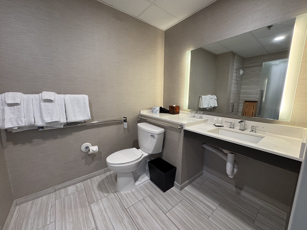 A hotel bathroom with a grab bar beside the toilet and a roll-under sink