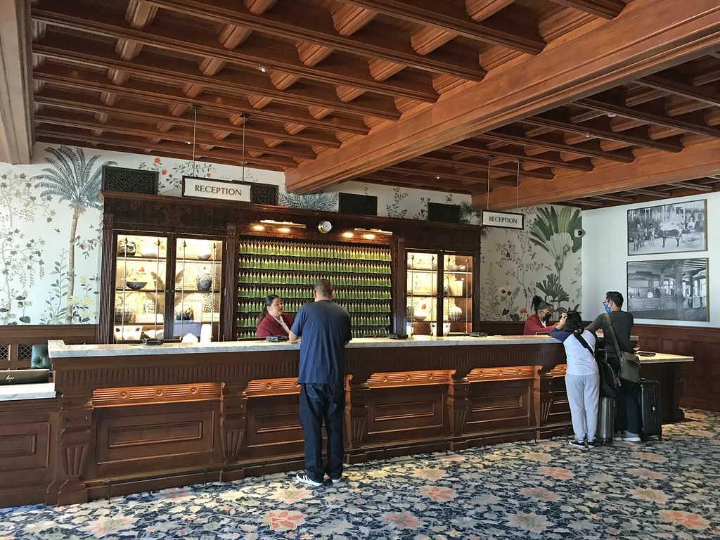 Guests at the reception desk of a hotel lobby with a carved wooden ceiling