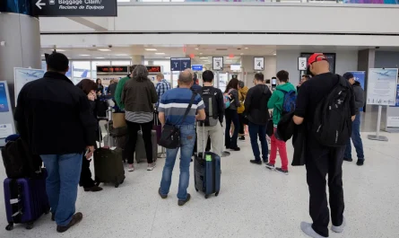 Travelers with rolling suitcases waiting in a line inside an airport terminal