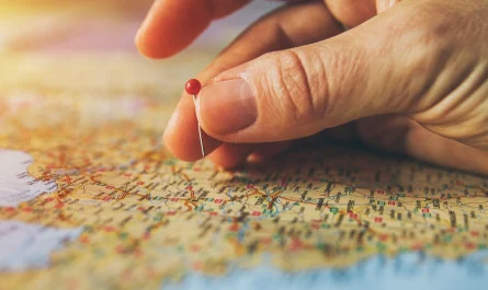 A hand placing a red pin on a colorful map