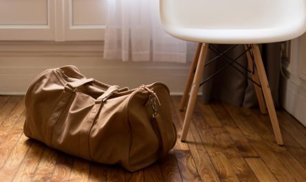 A tan duffel bag on a wooden floor beside a white chair