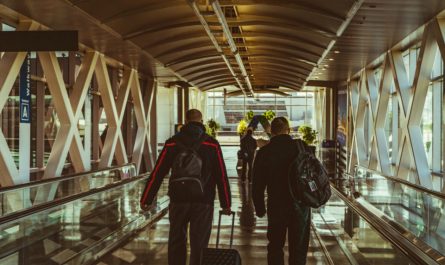 Two travelers with backpacks and a suitcase on an airport moving walkway