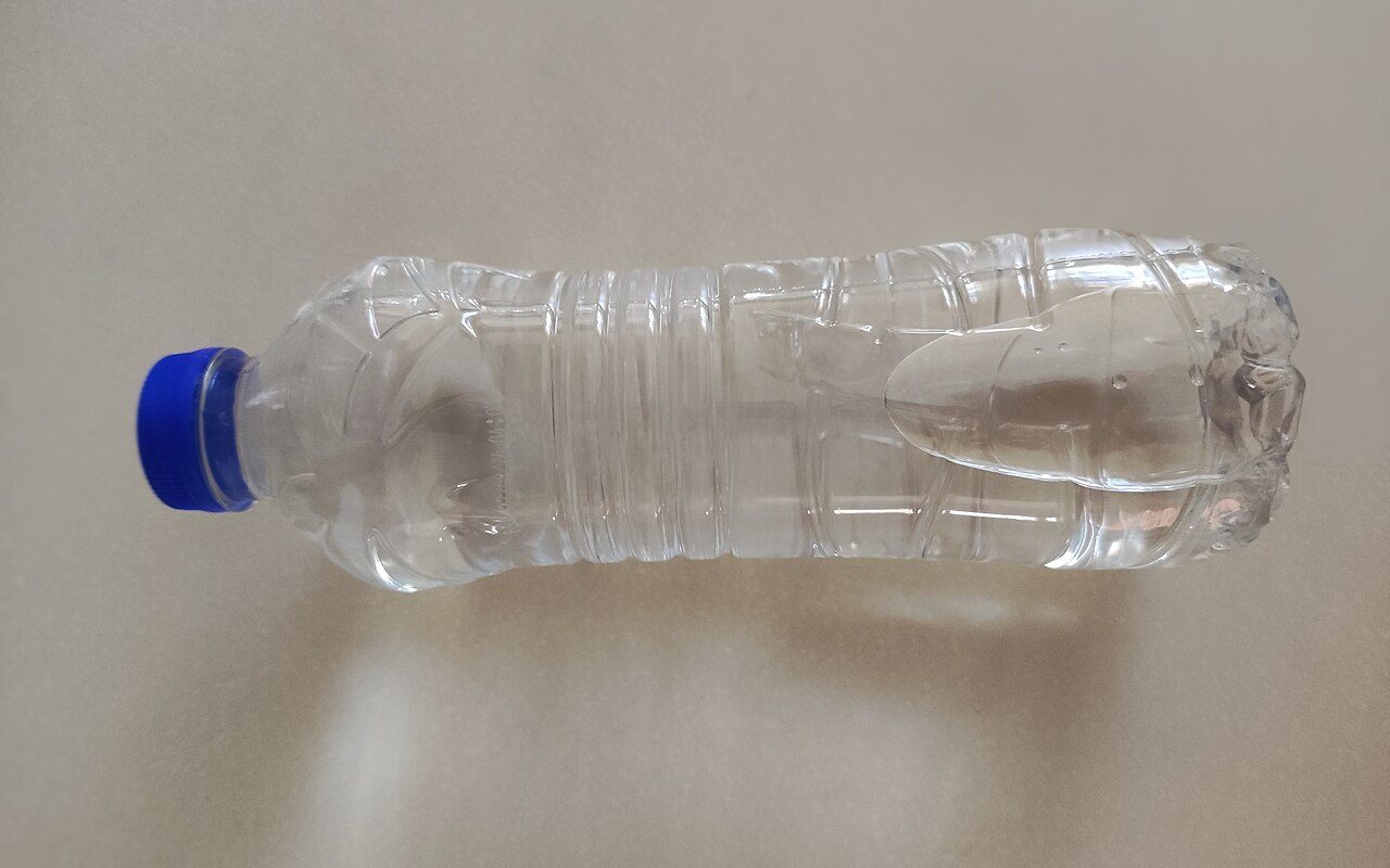A clear plastic water bottle with a blue cap lying on its side on a beige surface.